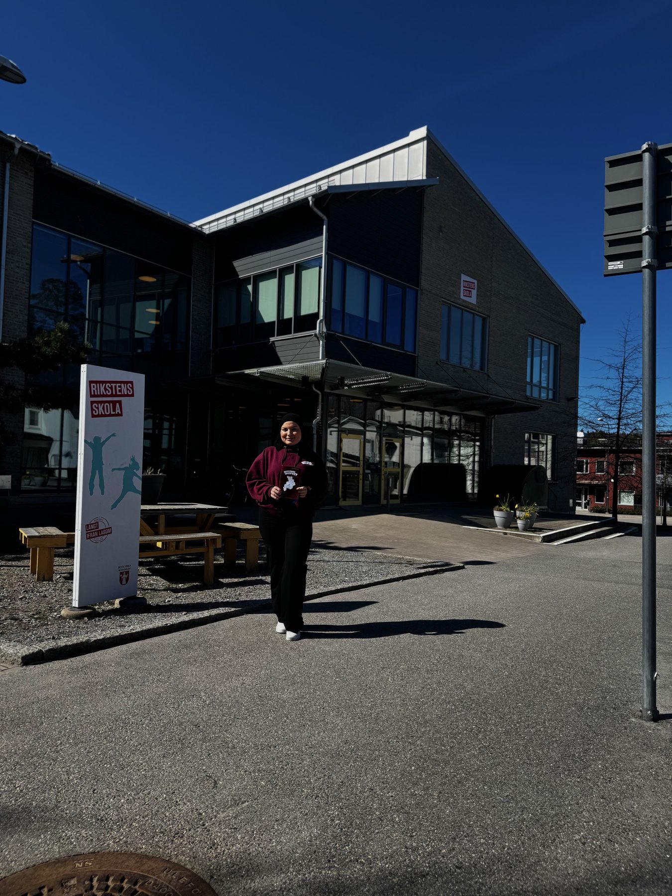 En medarbetare i Ordfest-hoodie framför Rikstens skola med Botkyrka kommuns skylt i förgrunden.